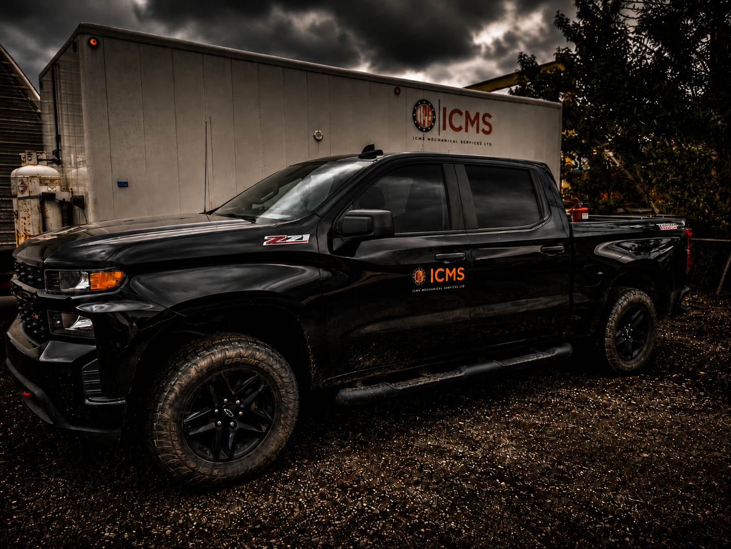 A black pickup truck with the ICMS logo parked outdoors under a dark, cloudy sky. The truck has off-road tires and is positioned in front of an industrial building with the ICMS Mechanical Services Ltd branding.