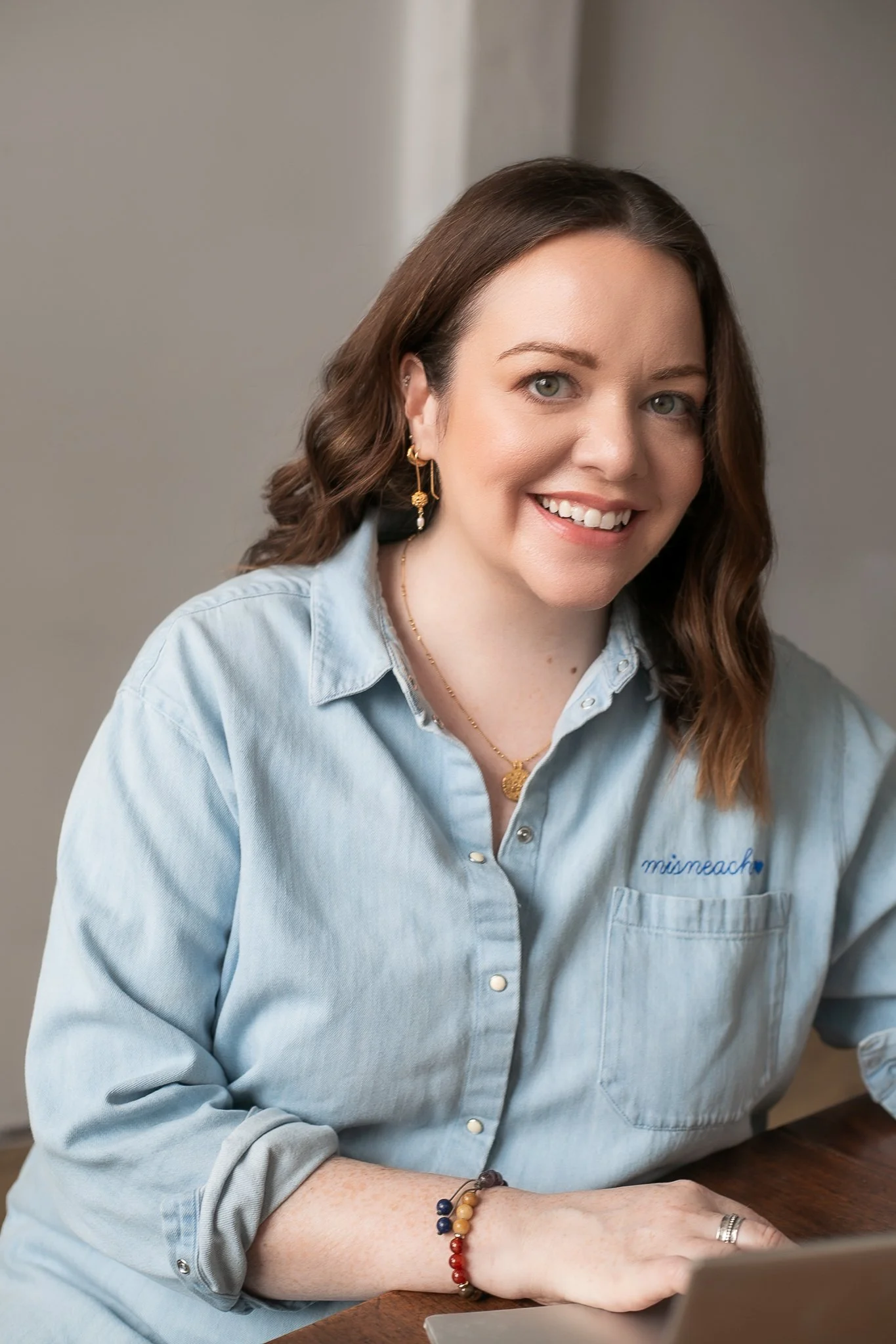 ADHD coach Aisling leaning forward with a warm smile, wearing a denim shirt with subtle Irish embroidery.