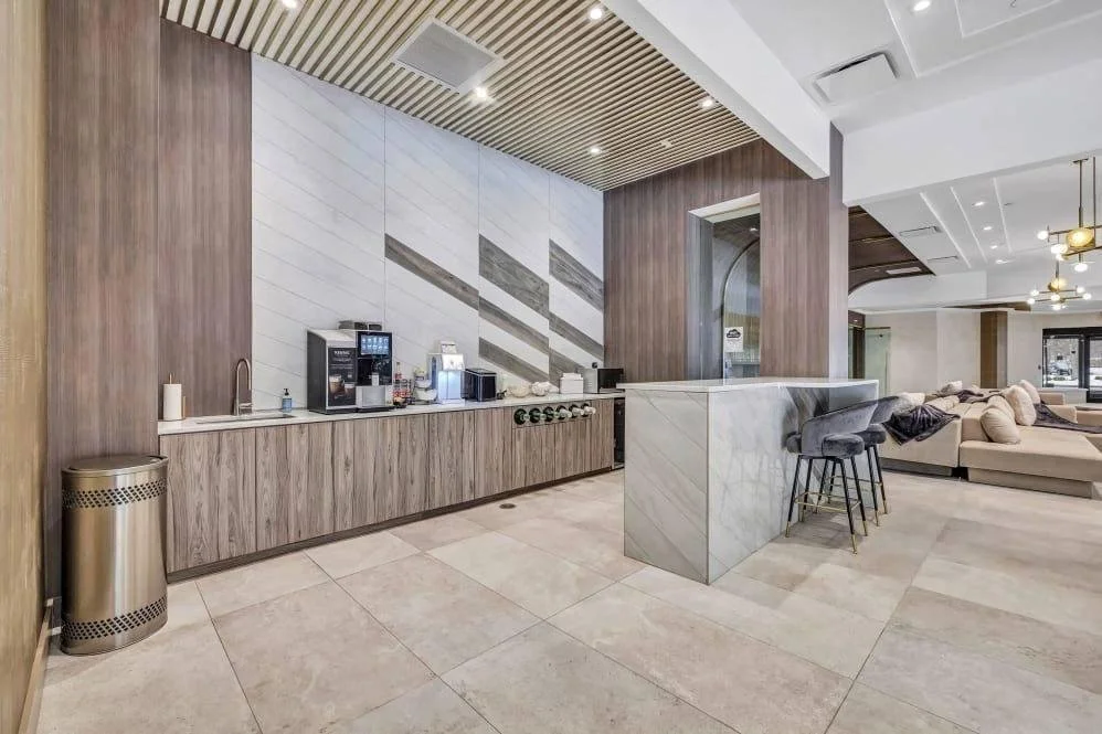 Modern lounge area with a coffee station, dark wood cabinetry, marble counters, and beige couches.