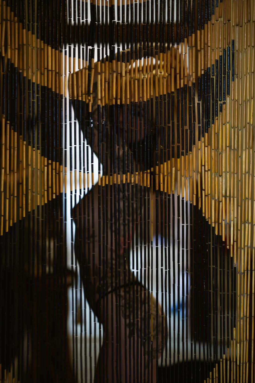 Close-up of a bamboo and black stick divider with a silhouette of a person behind it, visible through the gaps.