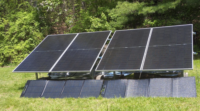 Multiple solar panels installed on a grassy field with trees in the background.