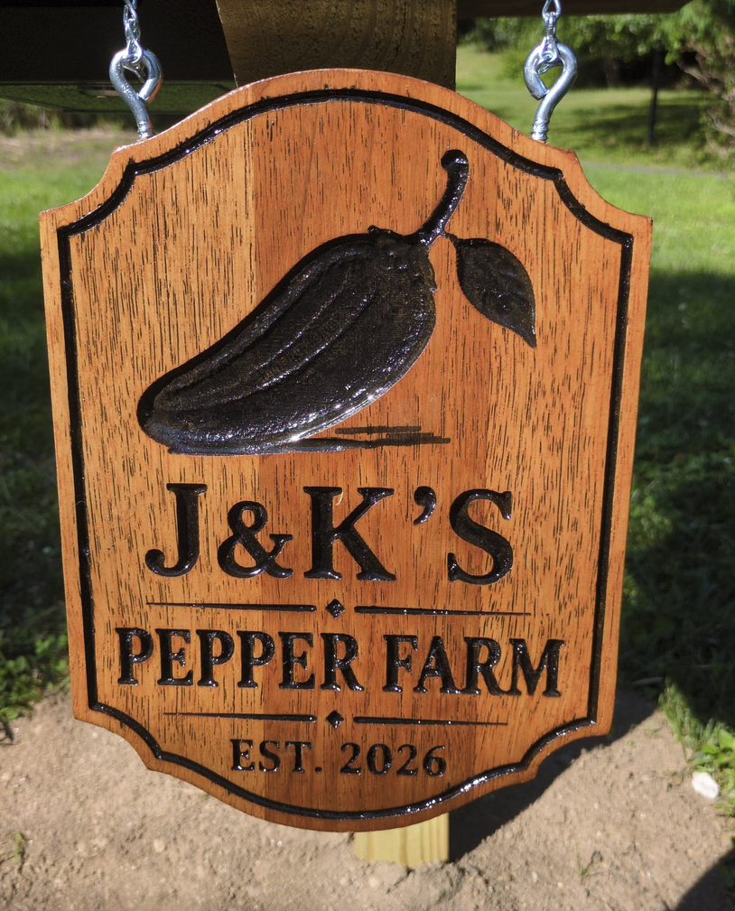 Wooden sign for J&K's Pepper Farm with a black pepper illustration, established in 2026, hanging outdoors.