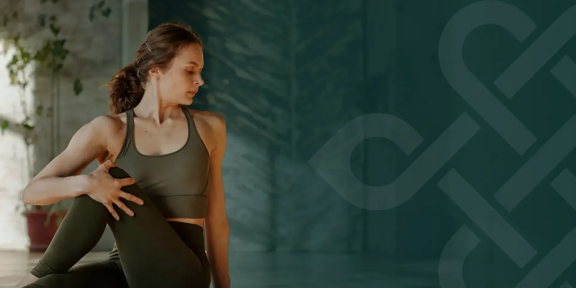 A woman performing a yoga pose indoors, stretching her back and chest while holding her foot with one hand.