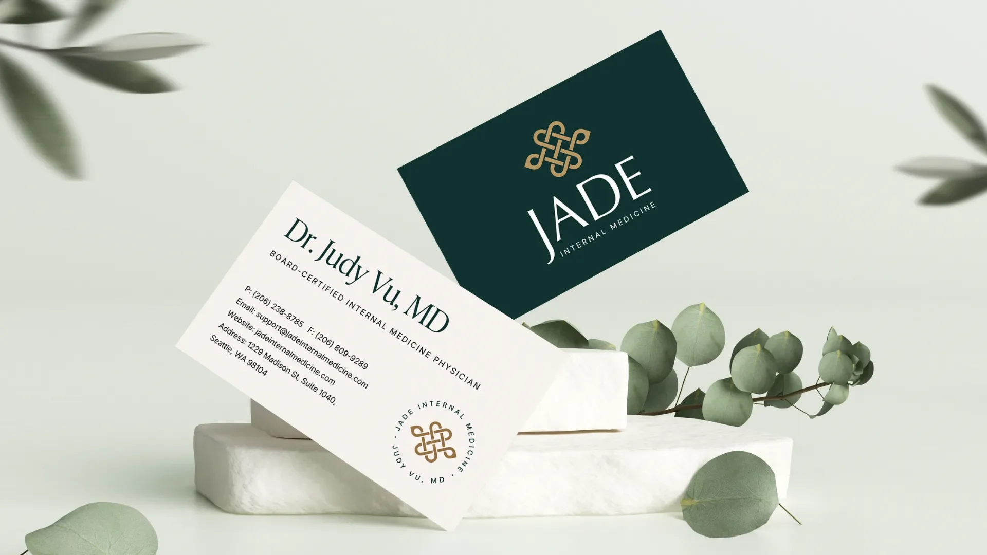 Business cards and a logo for Jade Internal Medicine, with eucalyptus leaves on a white display stand.