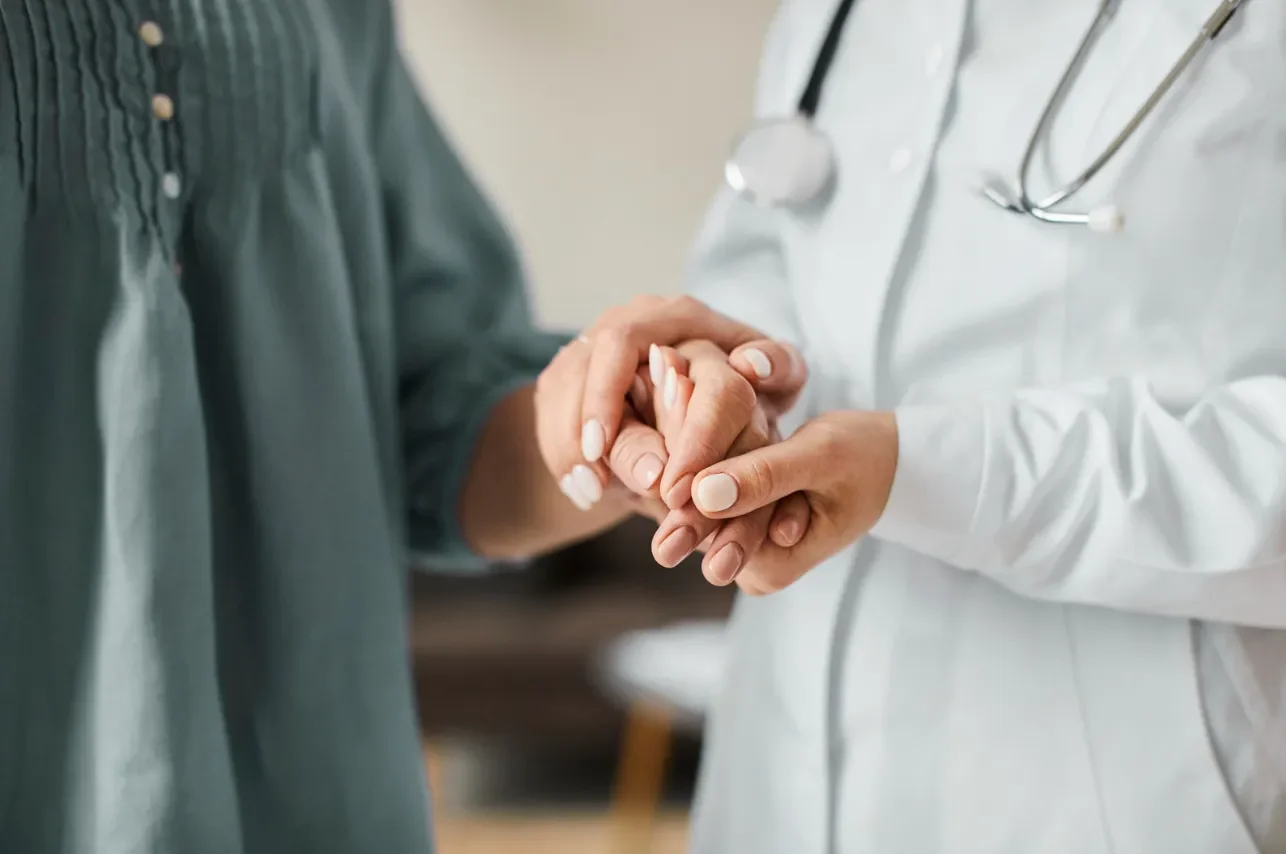 A healthcare professional in a white coat holding a patient's hand during a consultation or examination.