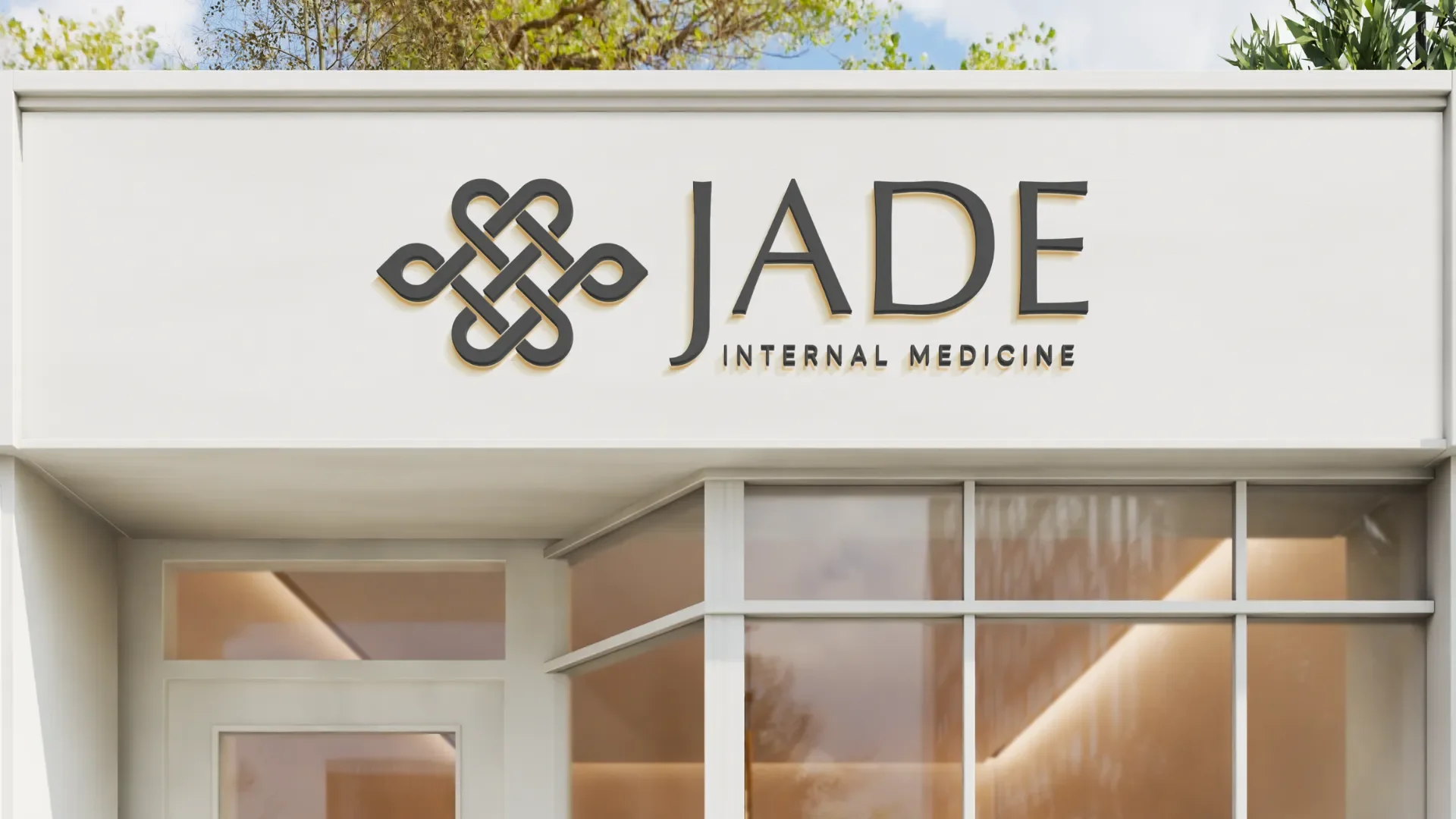 Exterior view of a building with a sign reading "JADE INTERNAL MEDICINE" and a decorative logo, trees and sky in the background.