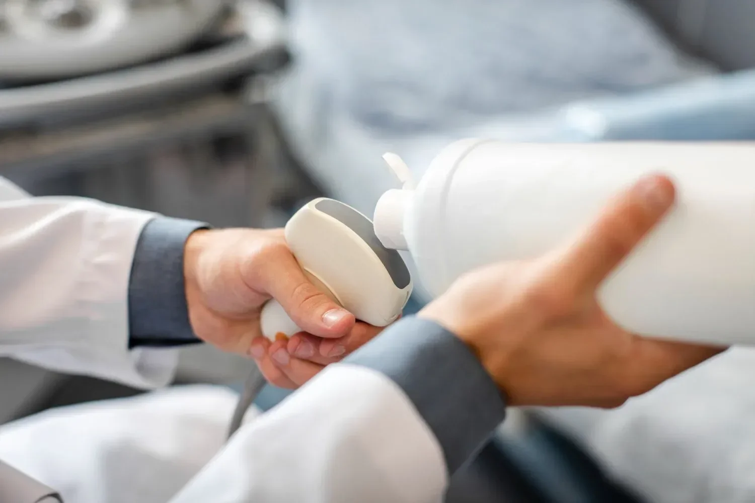 A person holding a white device, possibly a medical or laboratory instrument, with another person assisting in a clinical or research setting.