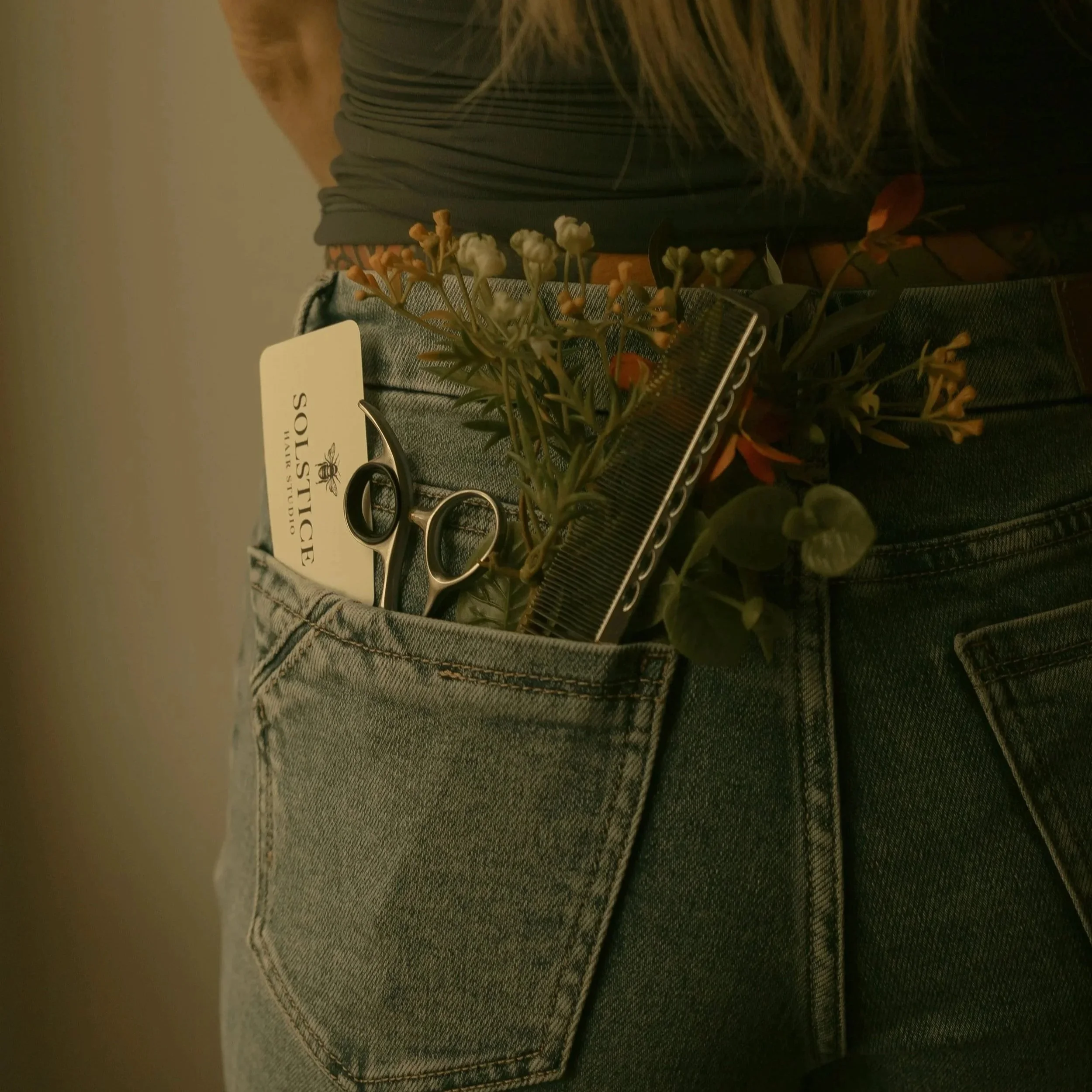Close-up of a person wearing grey denim jeans, with a floral arrangement and scissors in the foreground.