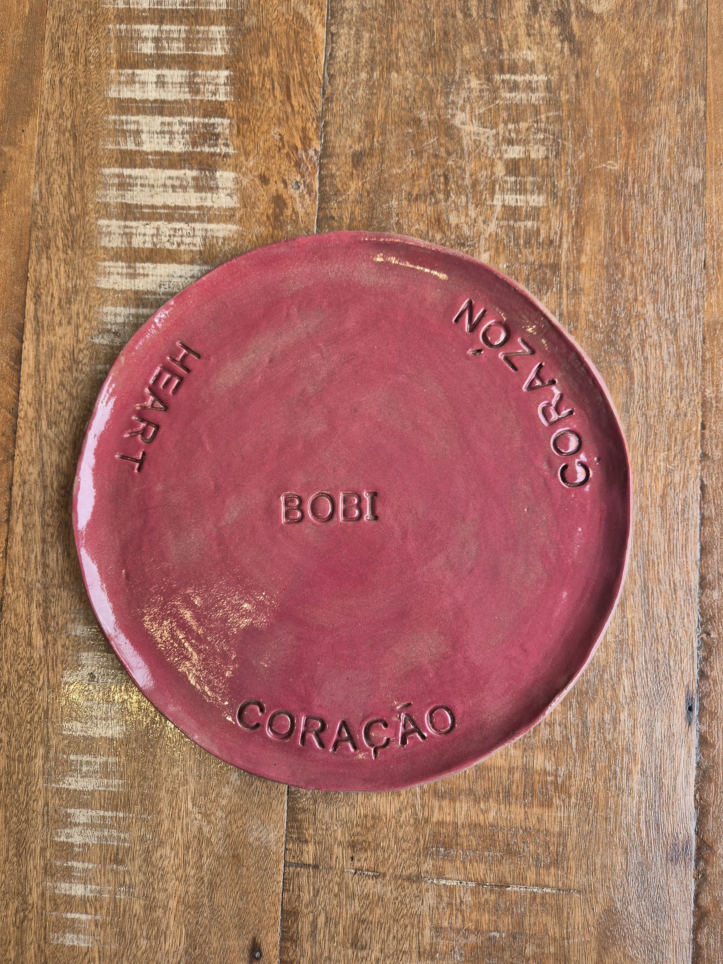 Prato de porcelana rosa com detalhes em letras e a palavra 'CORAÇÃO'.