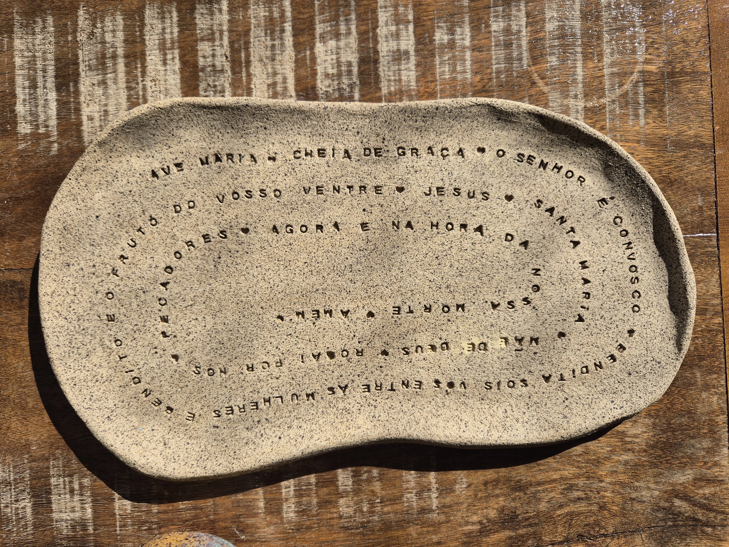A oração da Ave Maria percorre toda a superfície deste prato em uma espiral, transformando palavras em textura e presença.

Mais do que um objeto religioso, esta peça fala sobre aquilo que atravessa diferentes formas de espiritualidade: a confiança d