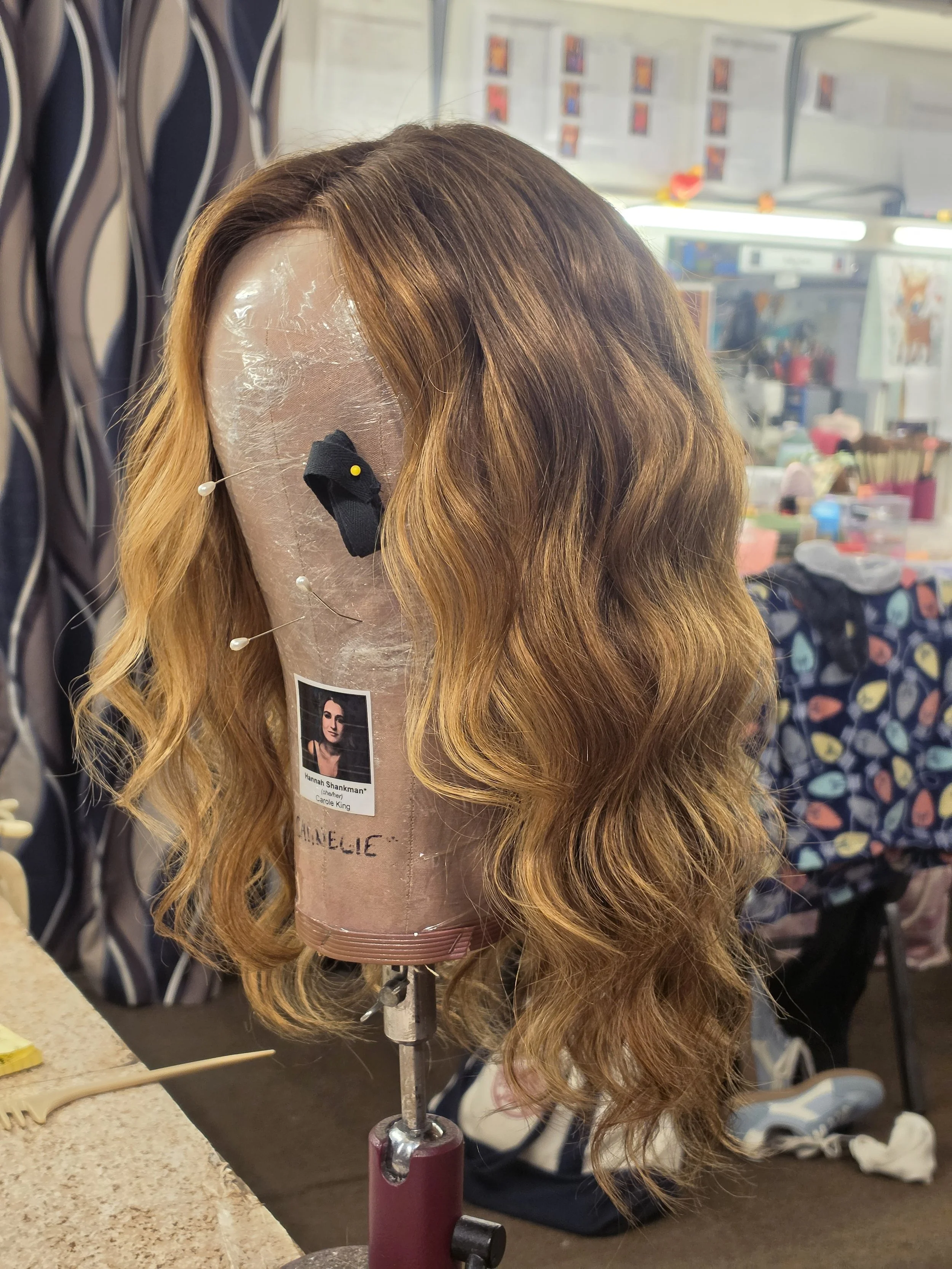 A mannequin head with long, wavy, reddish-brown hair on a wig stand in a salon or store setting.