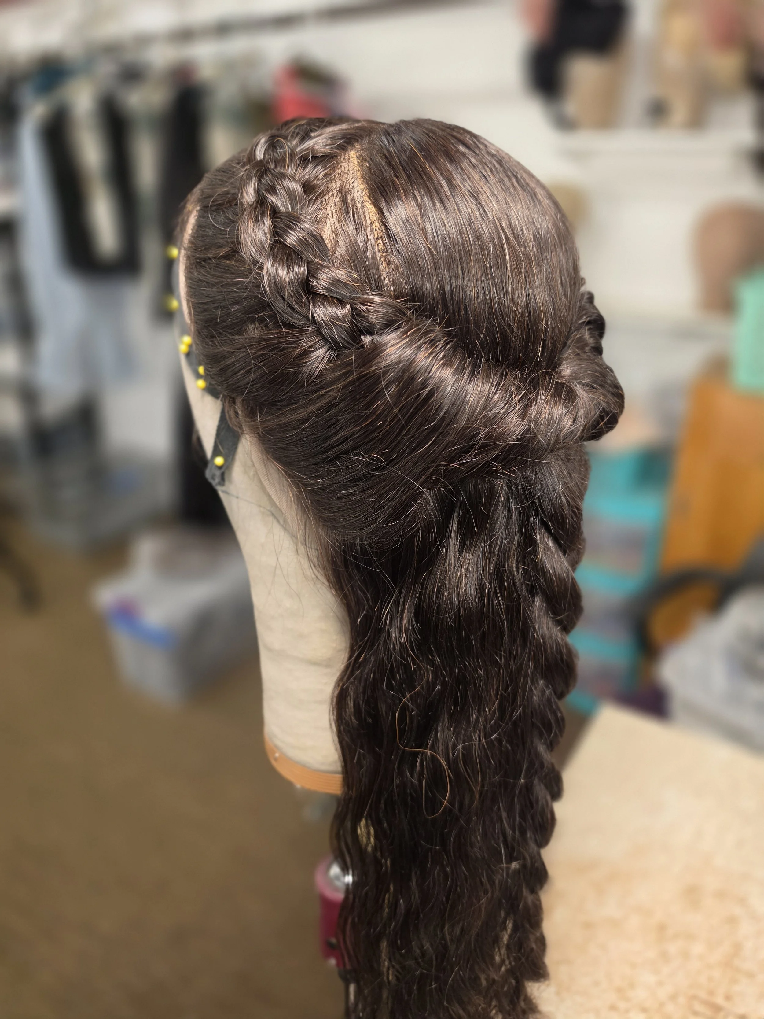 A wig styled with a French braid on one side and long wavy hair on the other, mounted on a mannequin head.