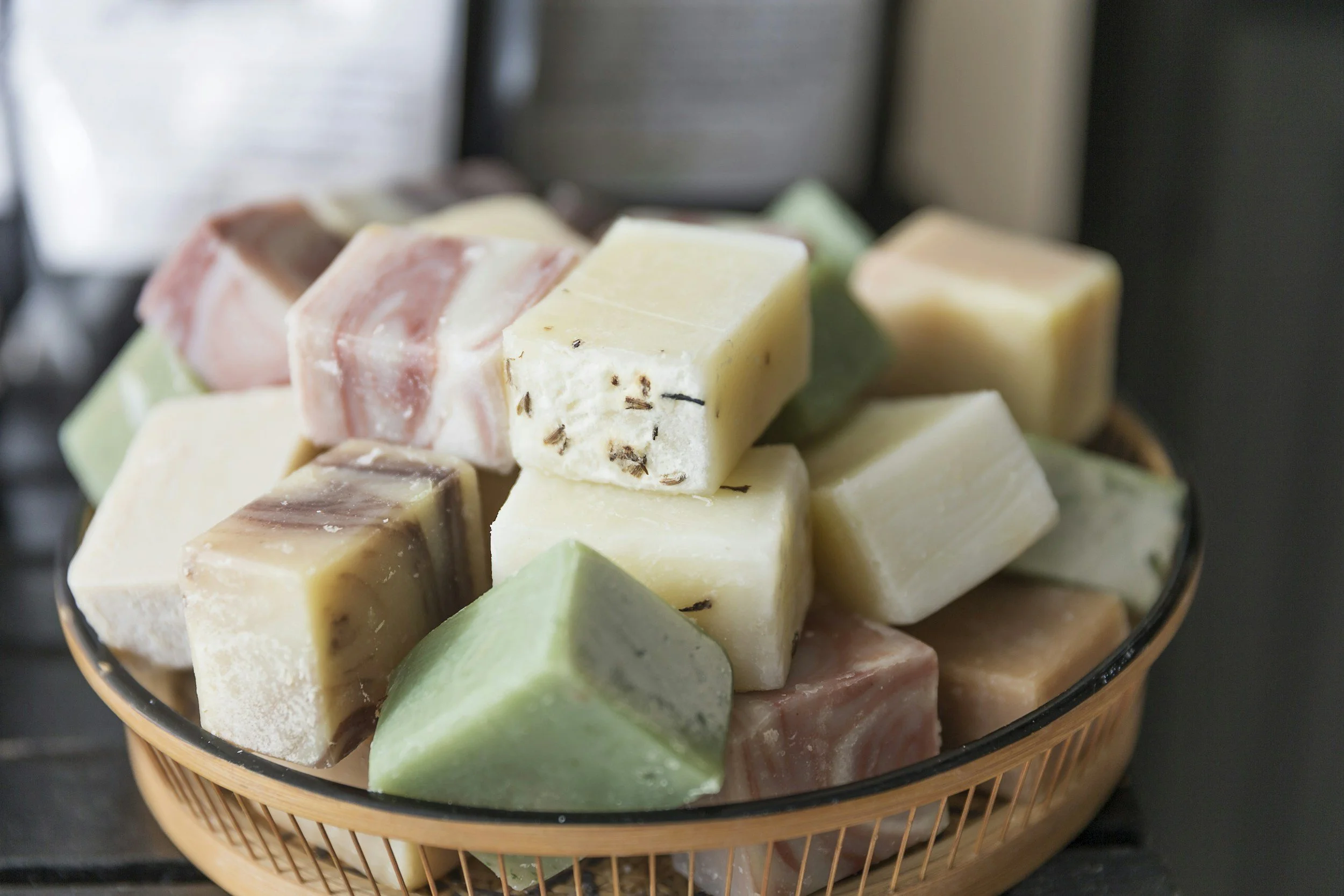 Assortment of handmade soap bars in various pastel colors in a woven basket.