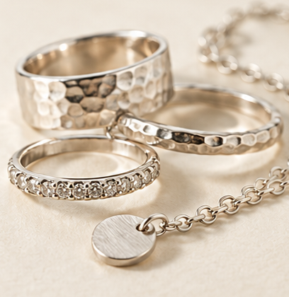 Collection of sterling silver rings featuring polished, textured and decorative finishes, arranged on a pale neutral background.