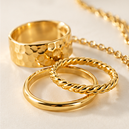 Collection of yellow gold rings featuring polished, twisted and hammered textures, arranged on a soft ivory background.