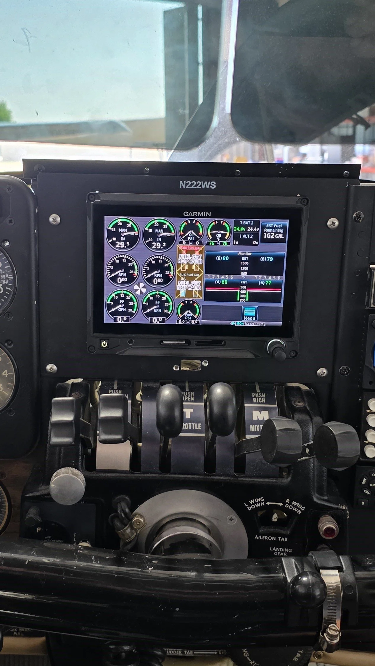 The image shows the cockpit of an aircraft with a Garmin flight display screen, various gauges, and controls, including throttle levers and switches.
