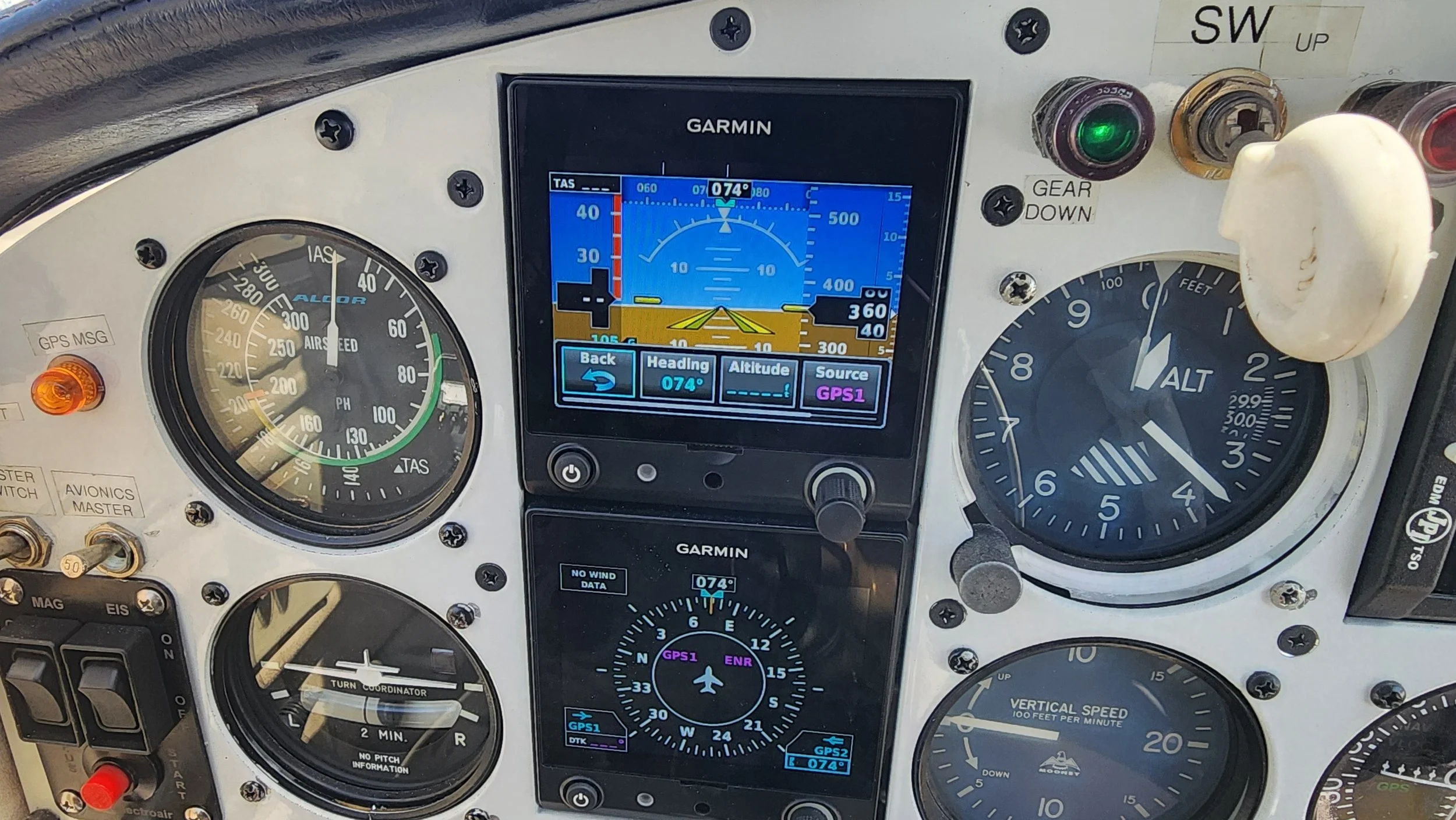 The image shows the cockpit of a small aircraft with various gauges and a GPS navigation screen in the center, displaying altitude, heading, and other flight data.