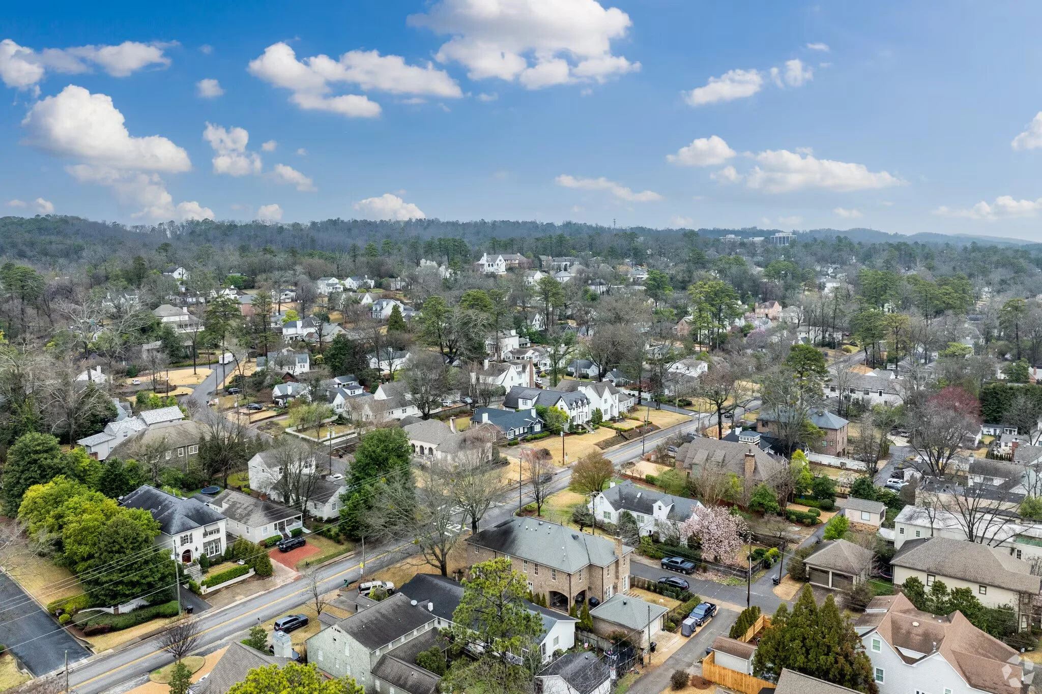 Aerial view of a suburban neighborhood with numerous houses, trees, and roads, under a partly cloudy sky.