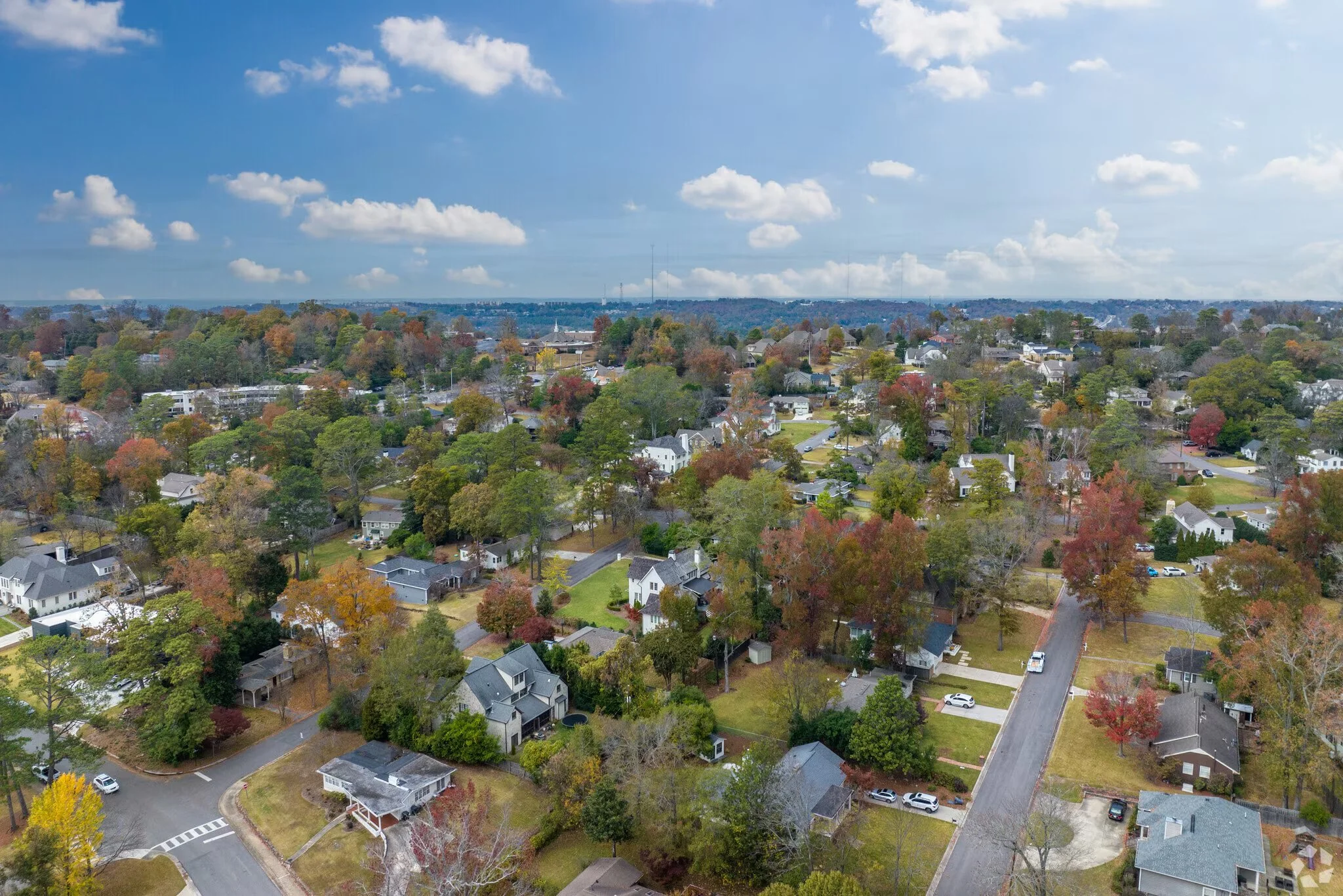 Aerial view of a suburban neighborhood with houses, trees, and streets under a partly cloudy sky during daytime.