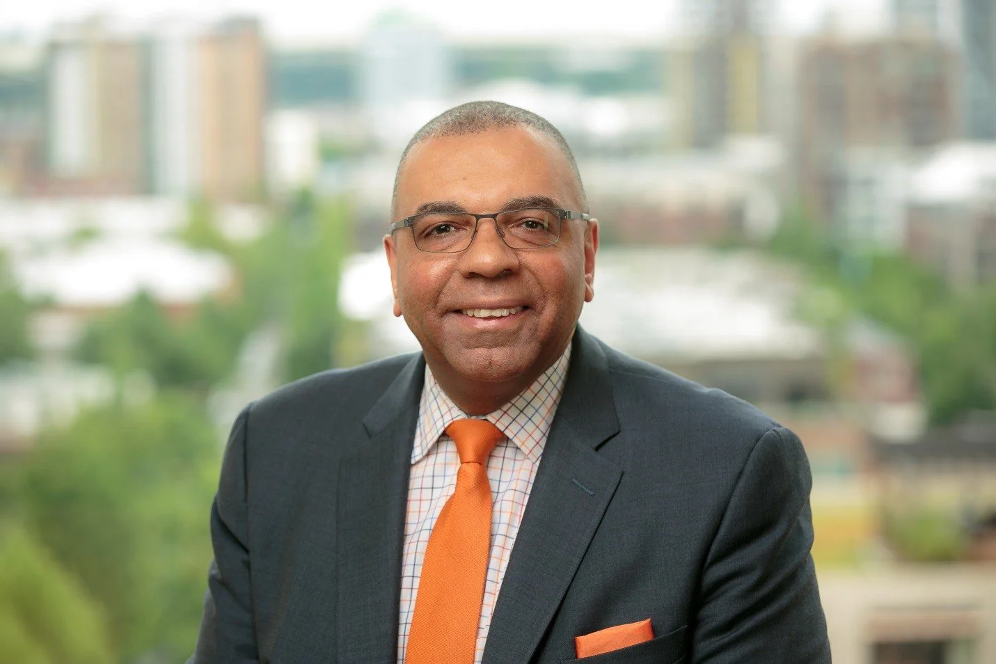 Vicente Pina in a gray suit and orange tie, the city behind him