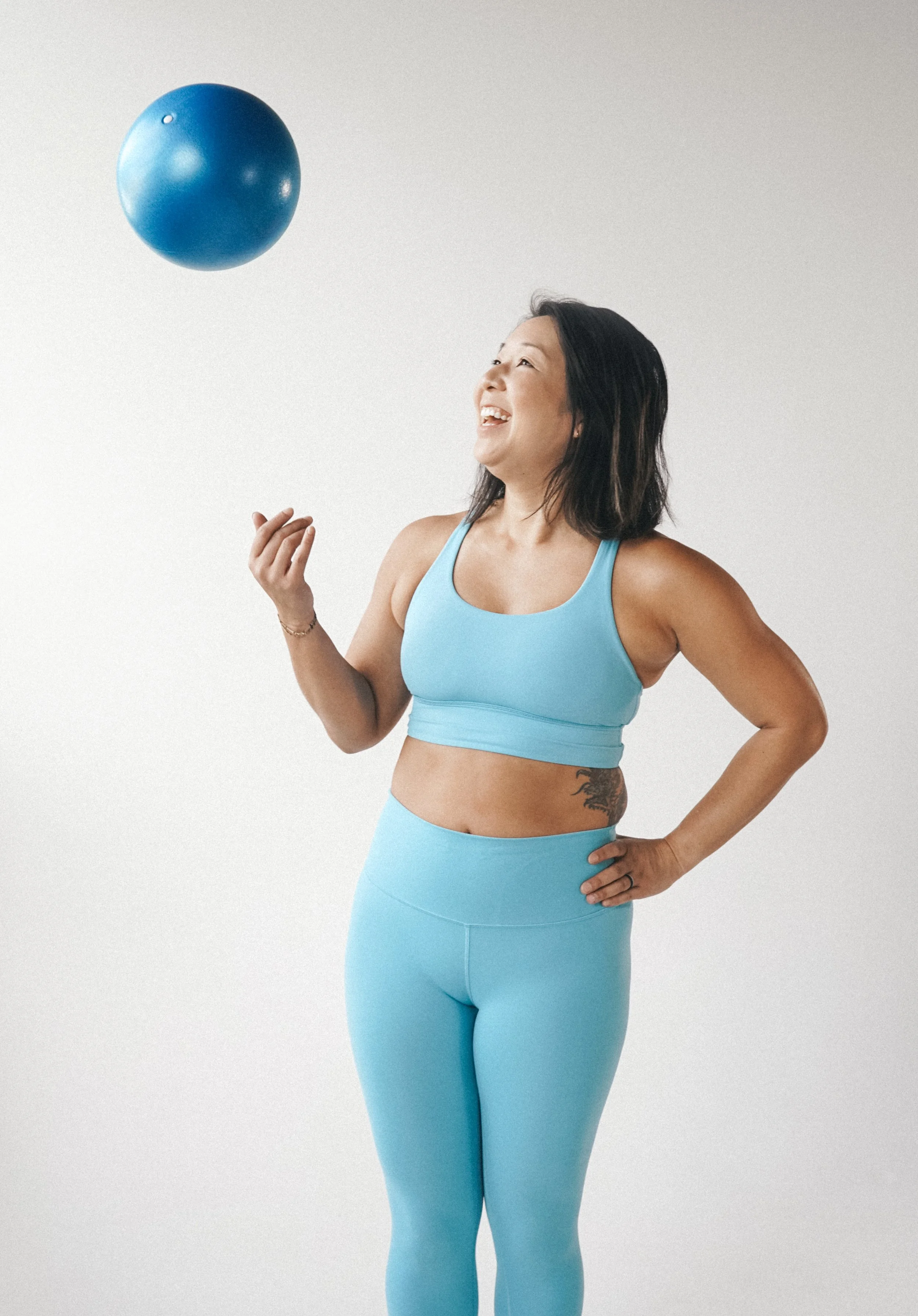 Woman in blue workout outfit holding a blue exercise ball and smiling.