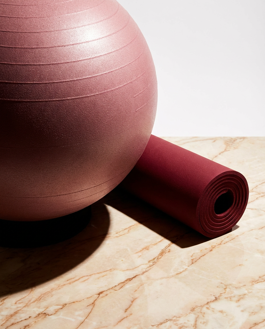 A pink exercise ball and a rolled-up red yoga mat on a marble surface.