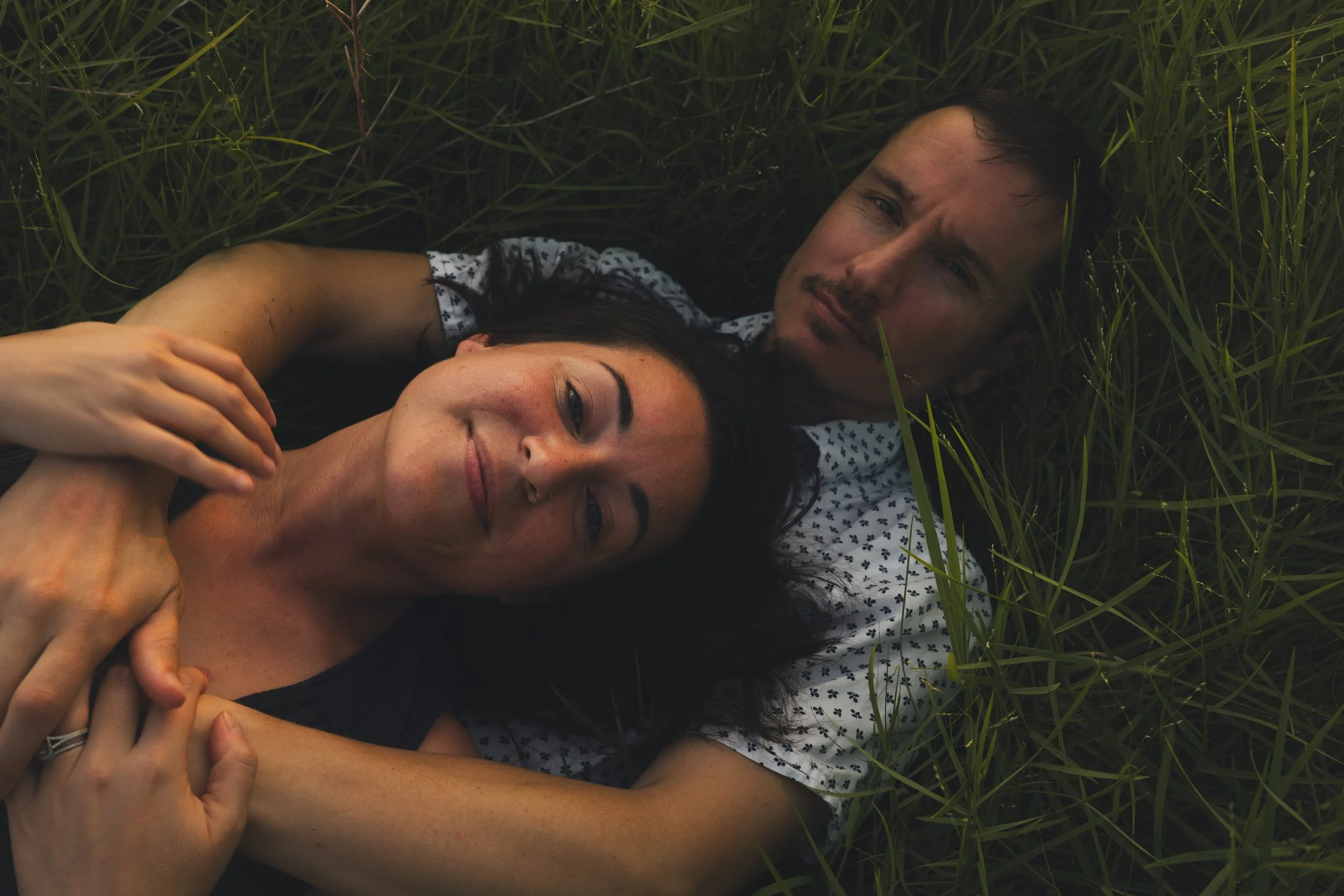 A man and woman lying on the grass, embracing each other and looking at the camera.