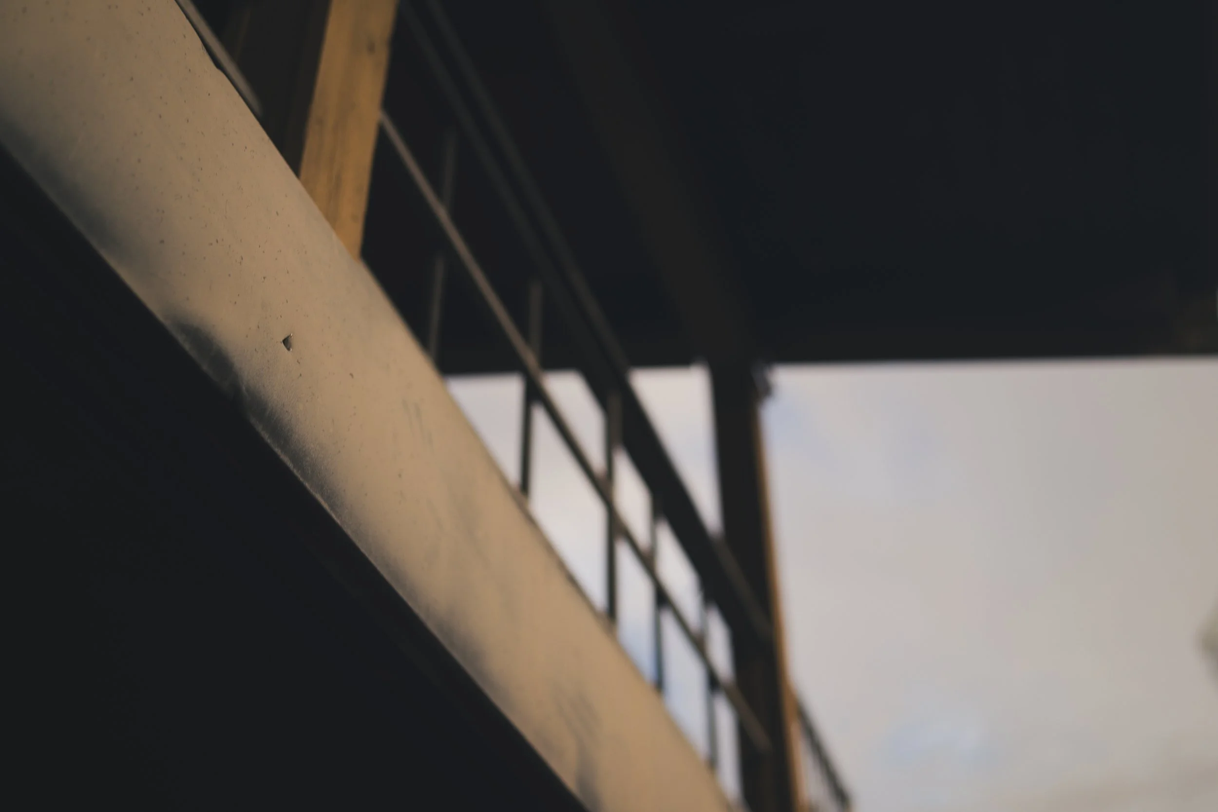 Close-up of a structure with vertical and horizontal beams, seen from below, with a dark background and a hint of cloudy sky.