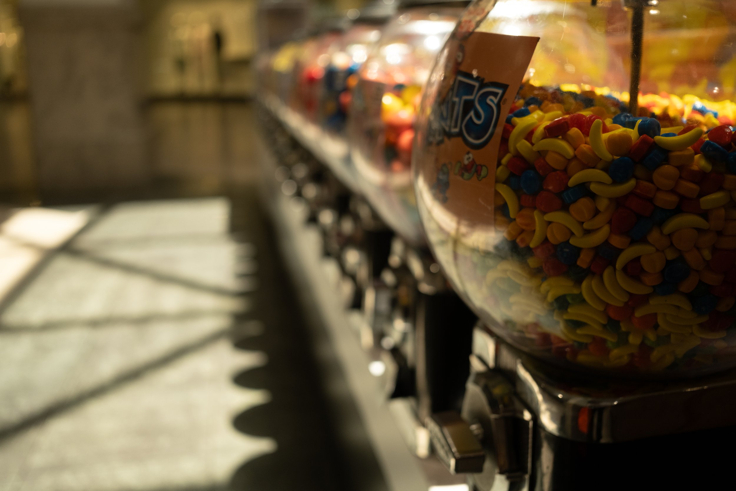 A row of candy jars filled with colorful candies, with a blurry background of a store or candy shop.