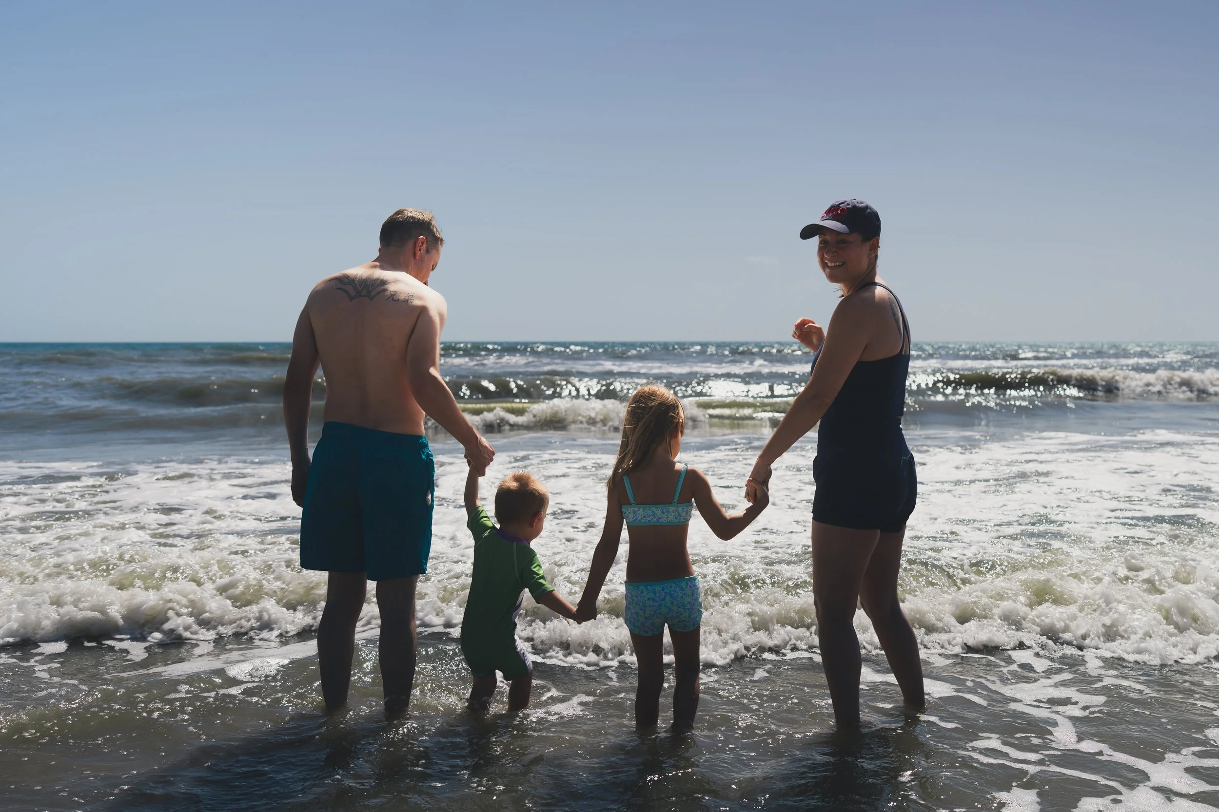 A family holding hands and playing in the ocean waves at the beach on a sunny day, with a clear blue sky.