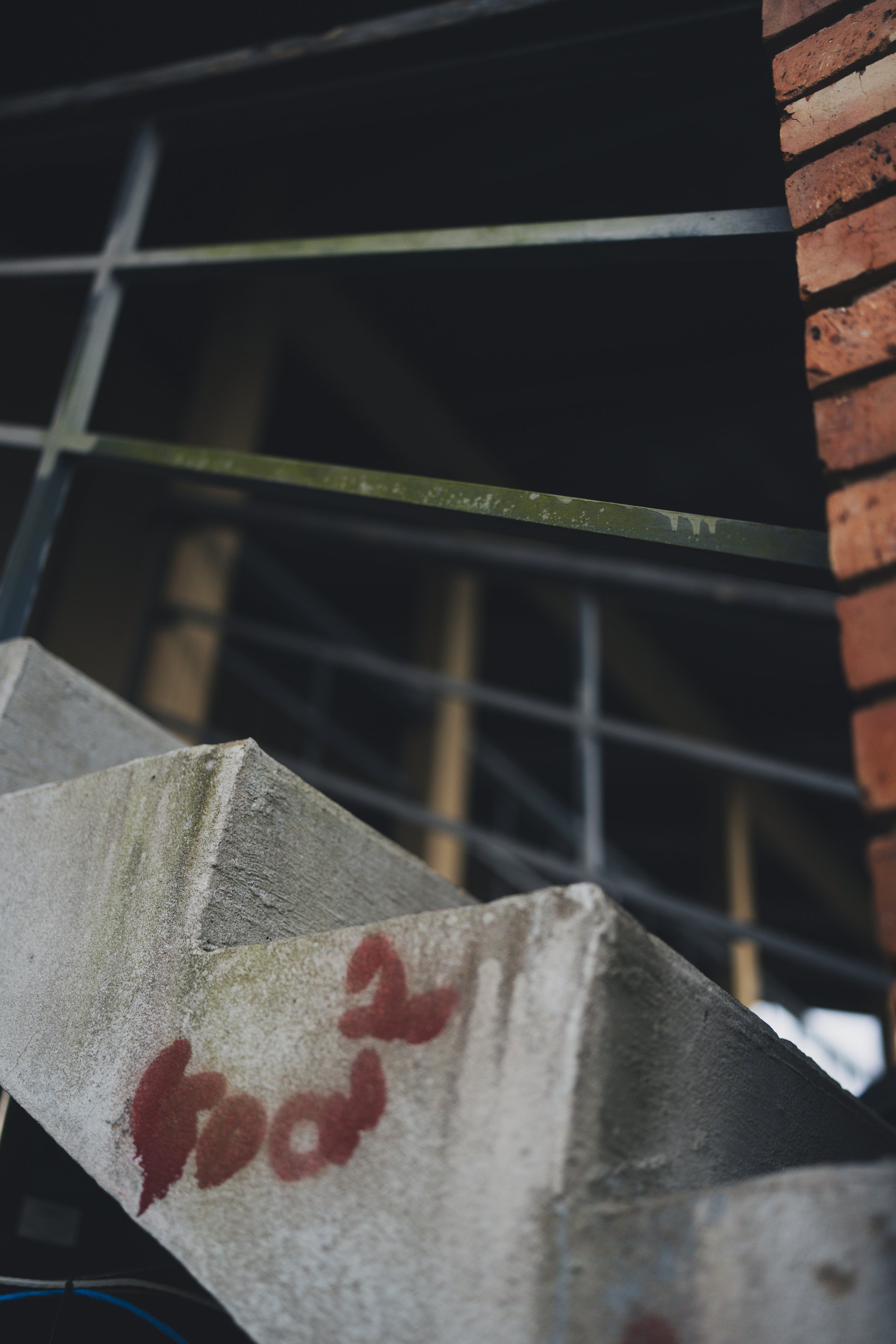 Close-up of graffiti on a rough, painted concrete surface with red spray paint and a worn brick wall in the background.