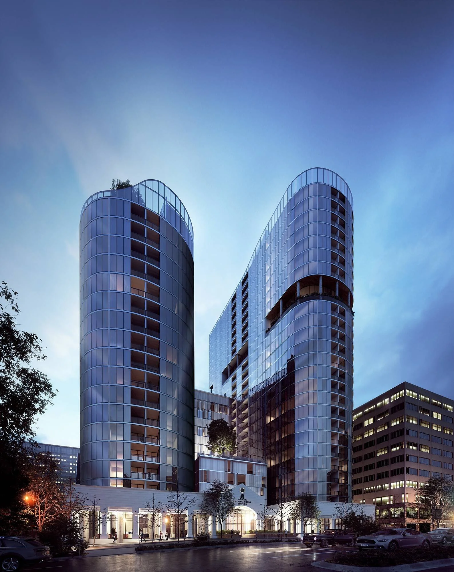 A modern high-rise building with curved glass facades at dusk, with trees and cars in front and illuminated ground-level entrance.