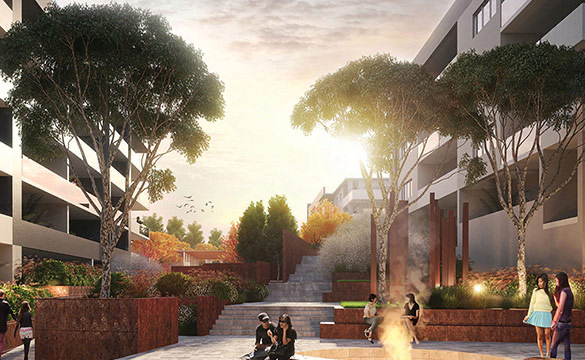 An outdoor urban park area surrounded by modern apartment buildings, with trees, stepped seating, and a small fire pit. People are sitting and walking around as the sun sets.