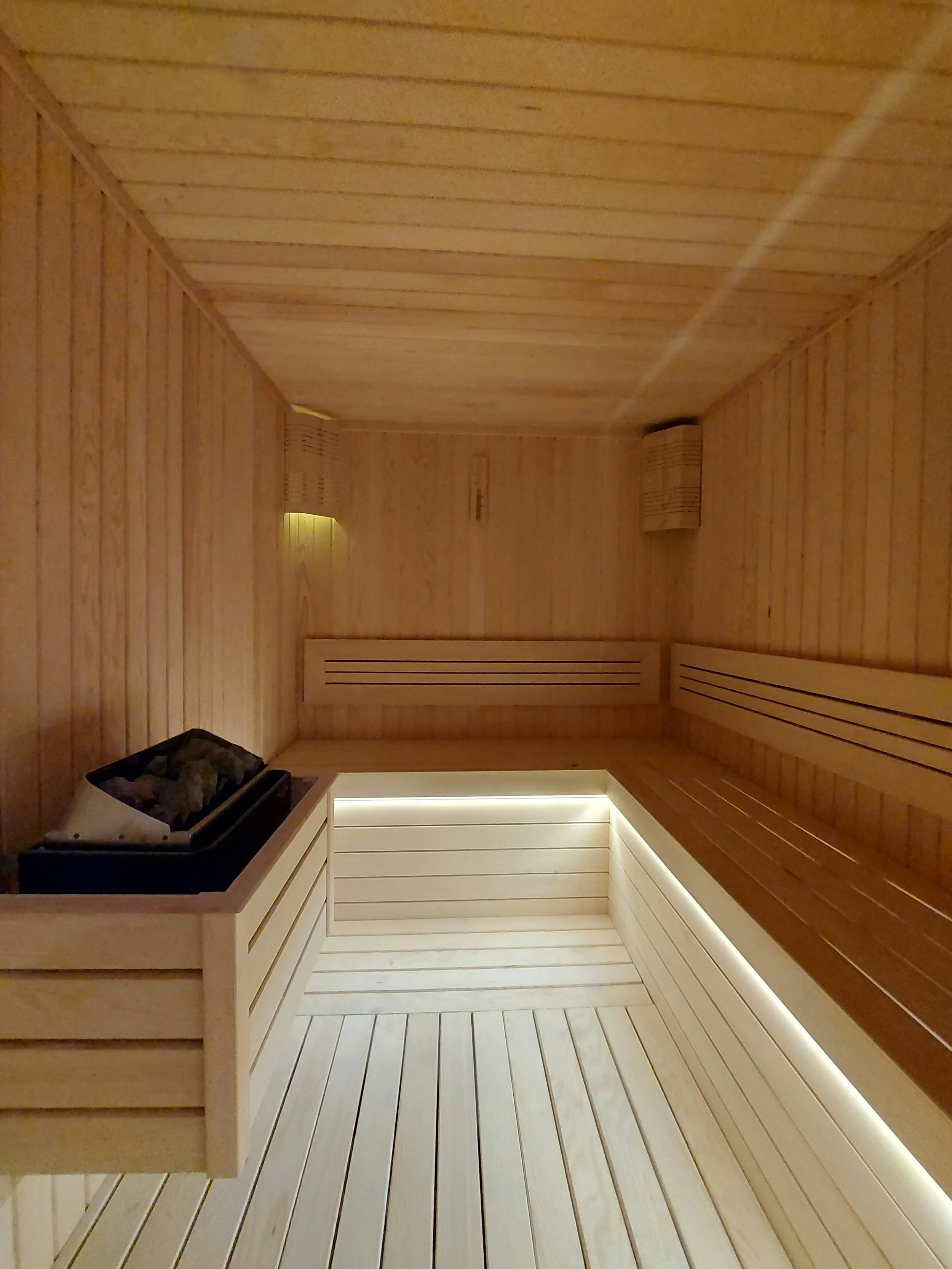 Wood-paneled interior of a sauna with benches and a heater in the corner