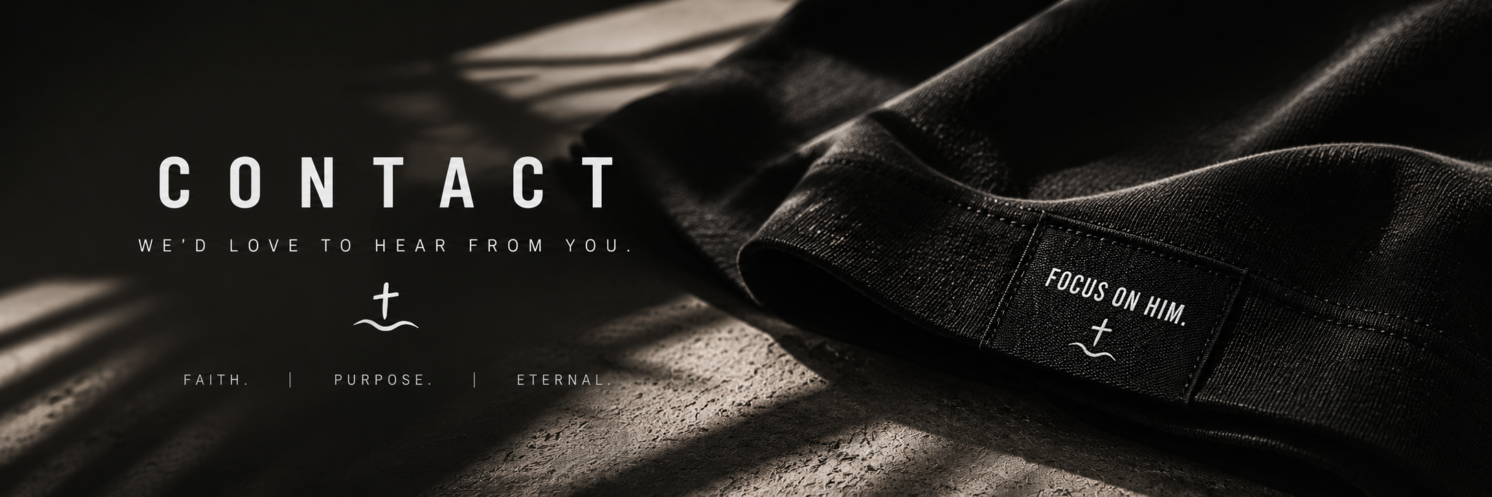 A black fabric garment with a tag reading 'Focus on Him' placed on a textured surface with shadows and light.