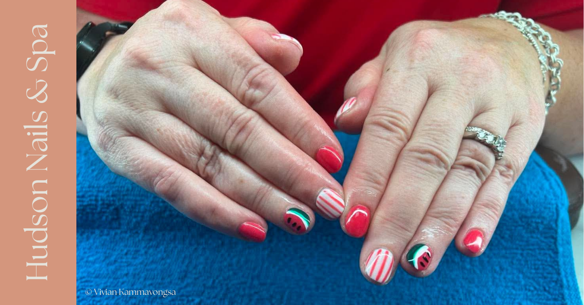 Close-up of hands with red and striped nail polish, a watermelon design on some nails, wearing rings and a bracelet, resting on a blue towel.