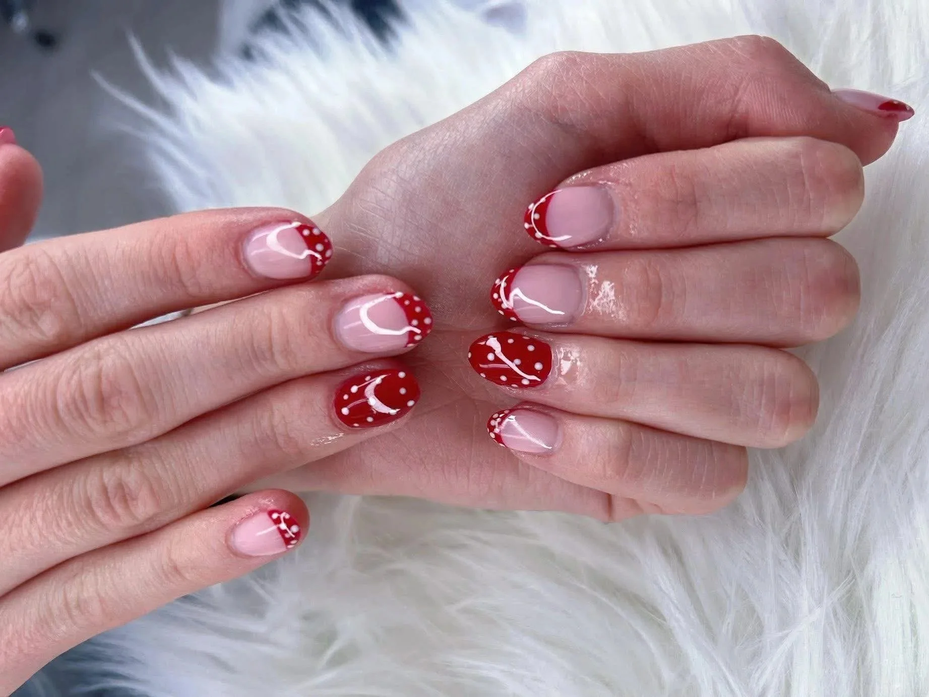 Close-up of a person's hands with manicured nails painted in a red and white polka dot pattern, resting on a fluffy white surface.