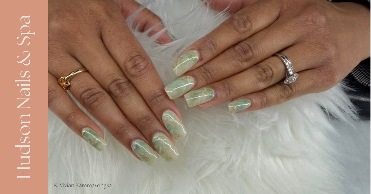 Close-up of hands with manicured nails in green marble design, wearing rings, resting on a white furry surface.