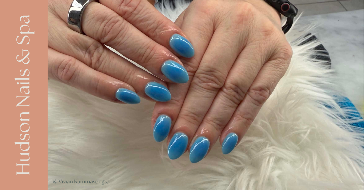 A person's hands with blue oval-shaped gel manicured nails resting on a white fluffy surface.
