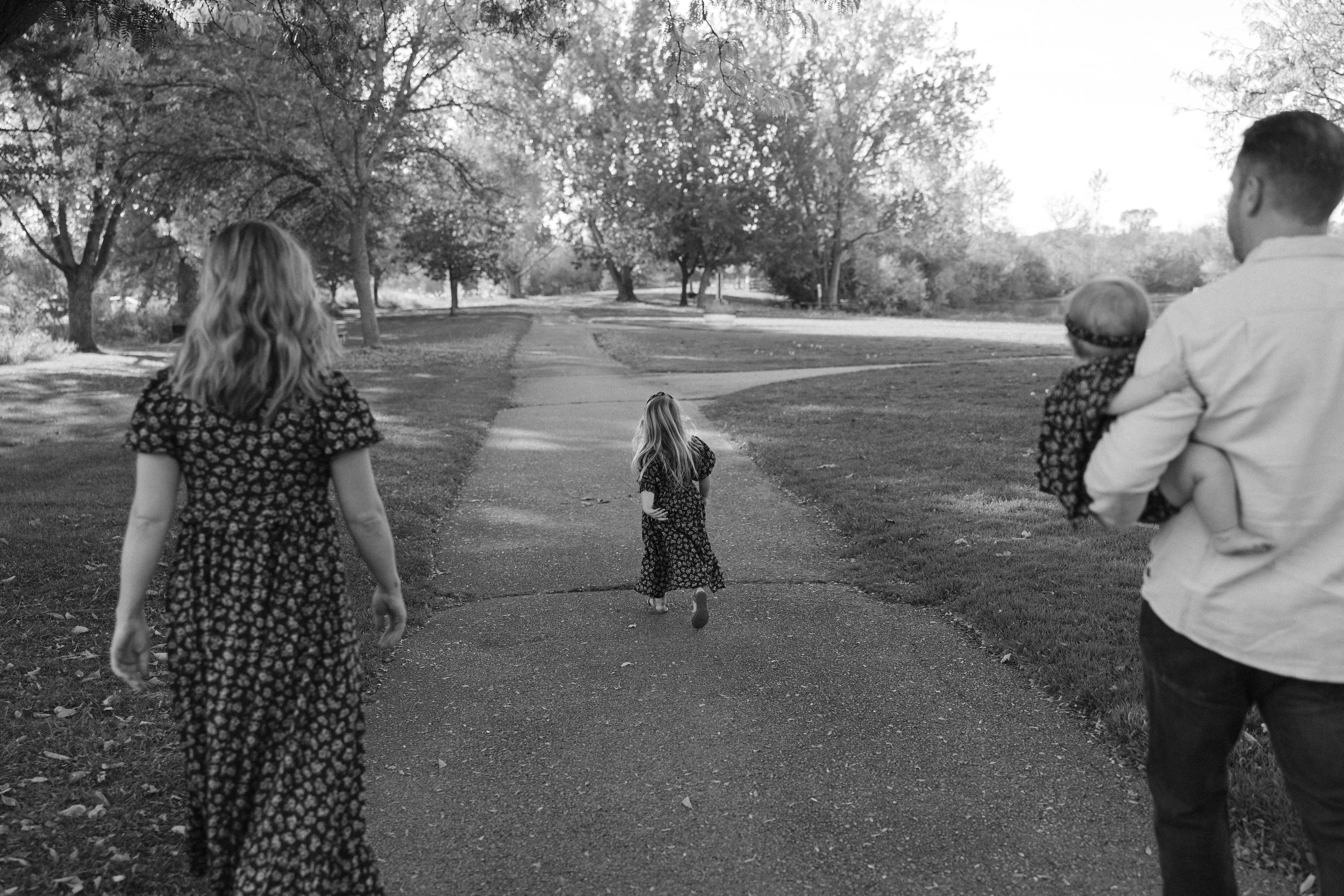 A black-and-white photo of a family walking in a park, children and adults, with trees lining the path.