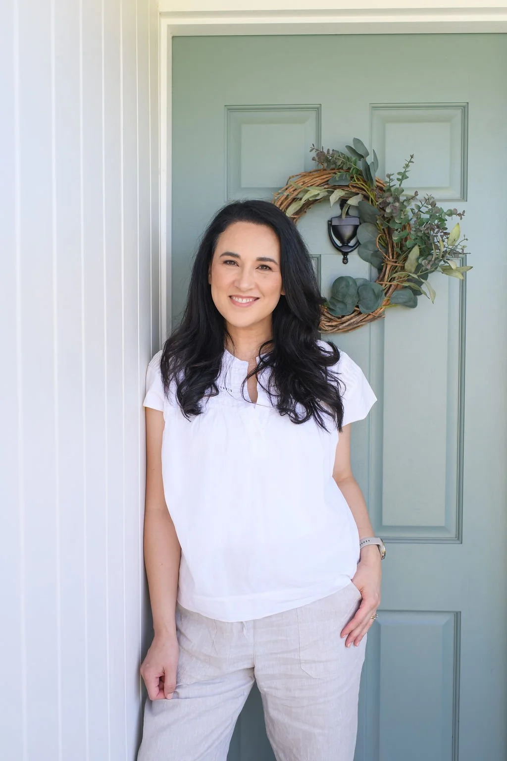 Christian artist and author, Jasmine Green, standing outside in front of a green door with a decorative wreath.
