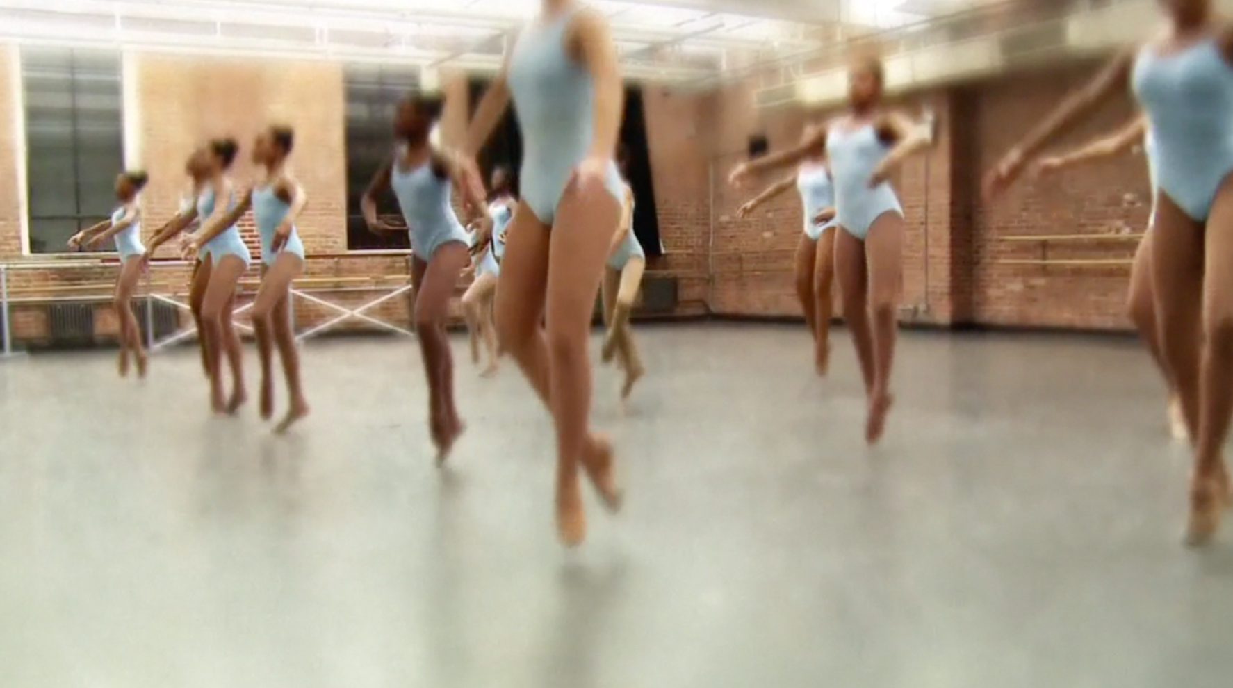 A group of ballet dancers practicing in a dance studio with brick walls and large mirrors.