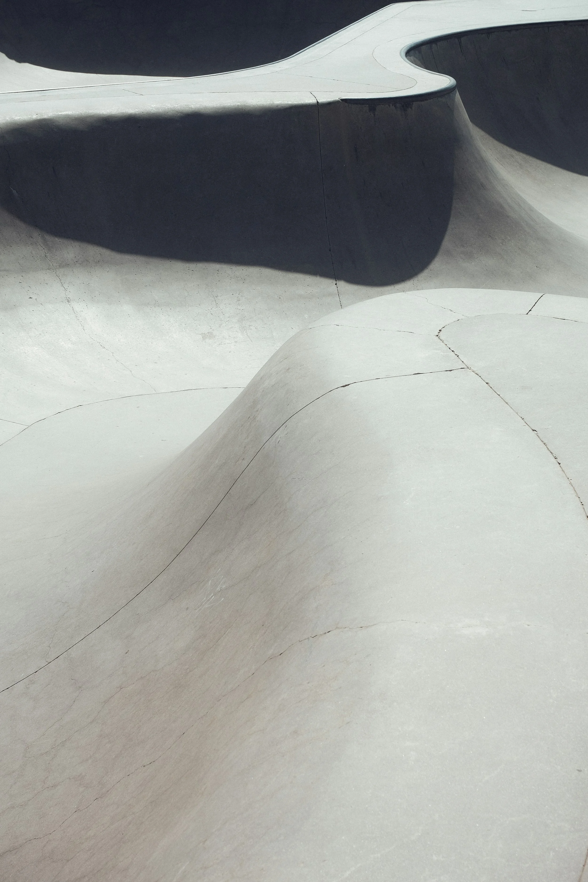 Concrete skatepark features smooth curves and ramps with shadows cast over the surfaces.