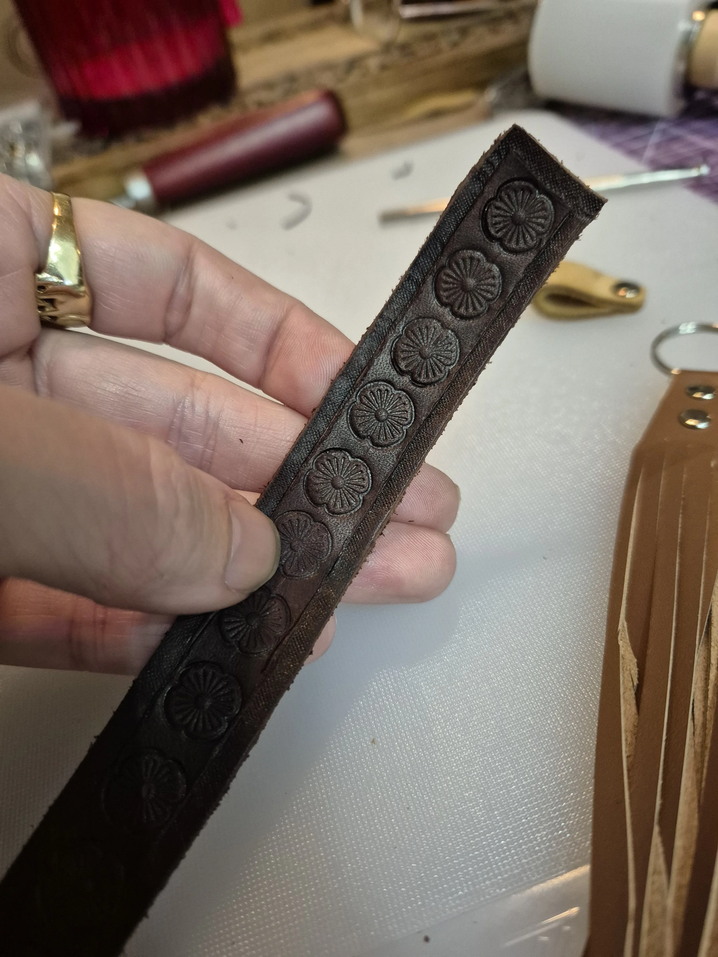 A person's hand holding a piece of dark leather with embossed floral patterns.