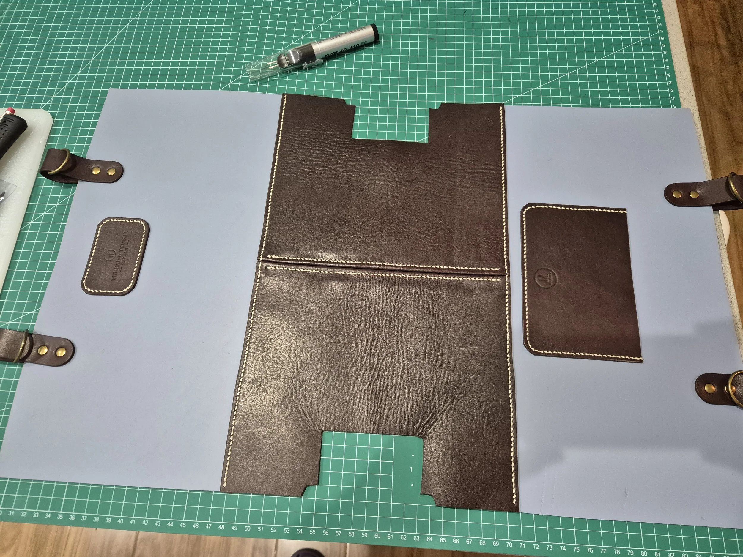 A crafting workspace with green cutting mat, leather pieces, and tools for making a leather bag.