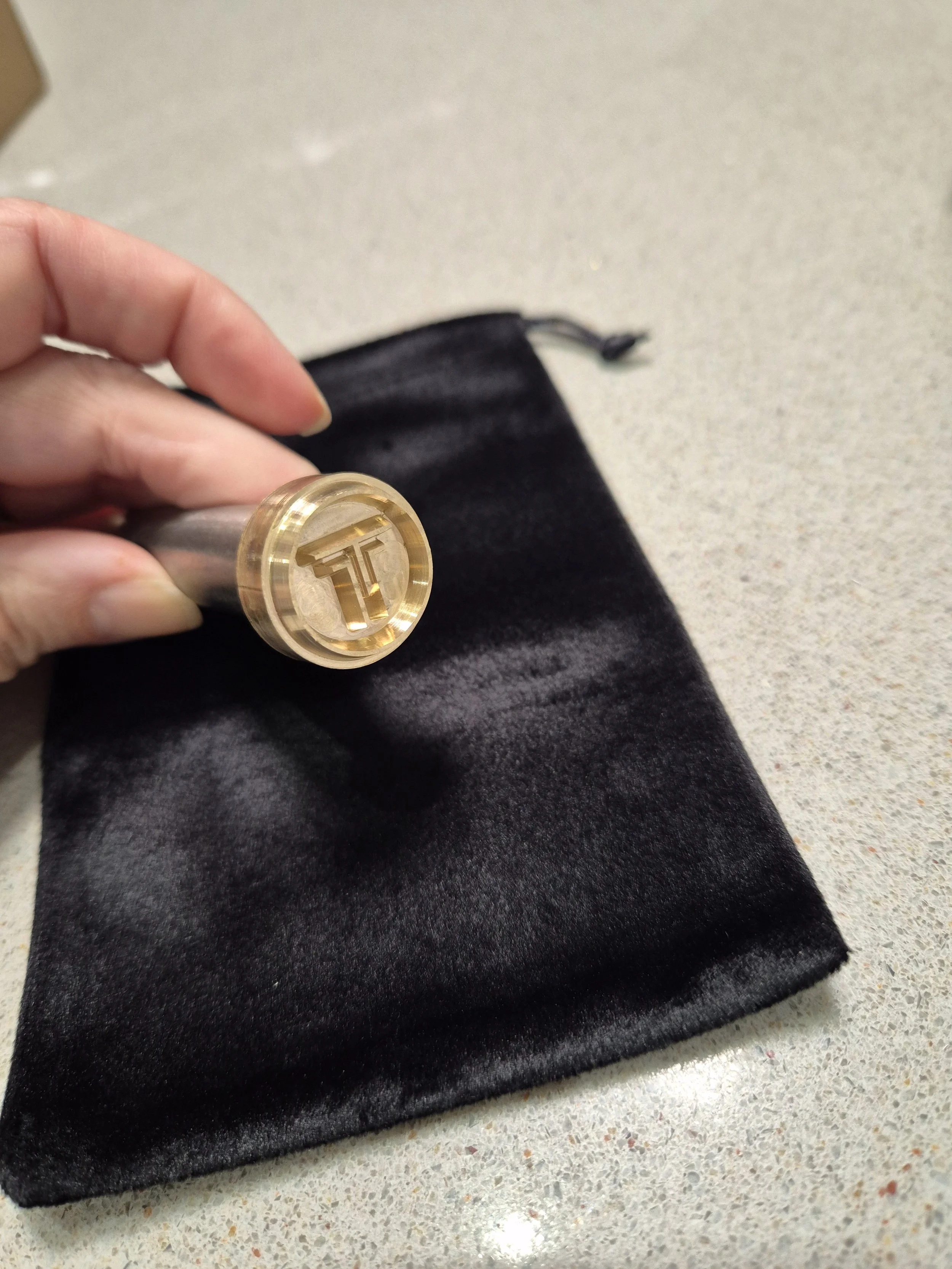A person holding a gold-colored coin with a 'T' symbol on it, resting on a black velvet cloth on a speckled countertop.