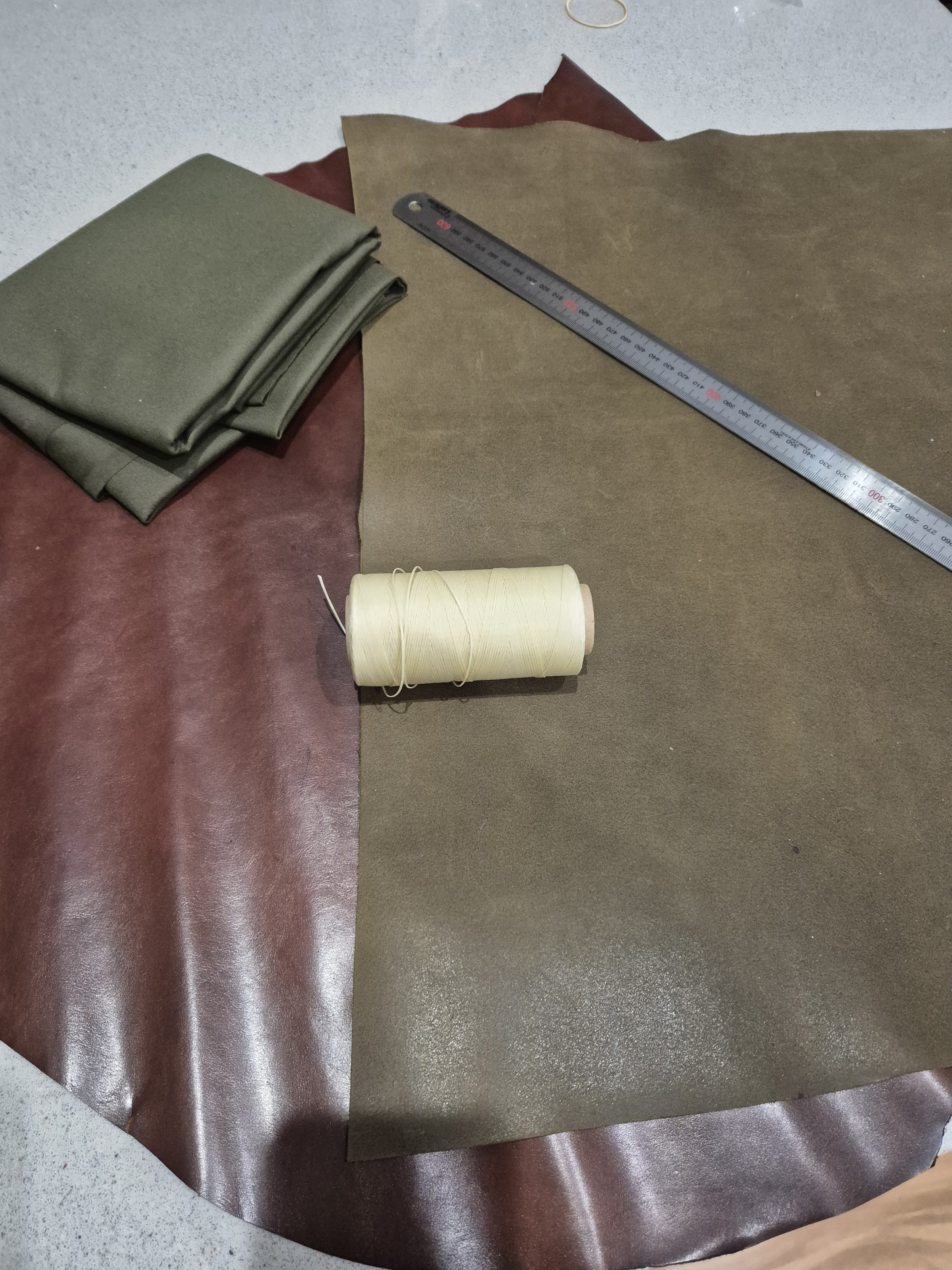 Various pieces of leather in different colors, a ruler, and a spool of thread, likely for sewing or crafting.