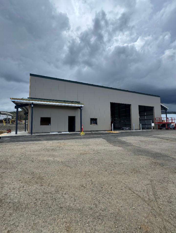 Front view of a large industrial building with a sloped roof, two large open garage doors, and cloudy sky.