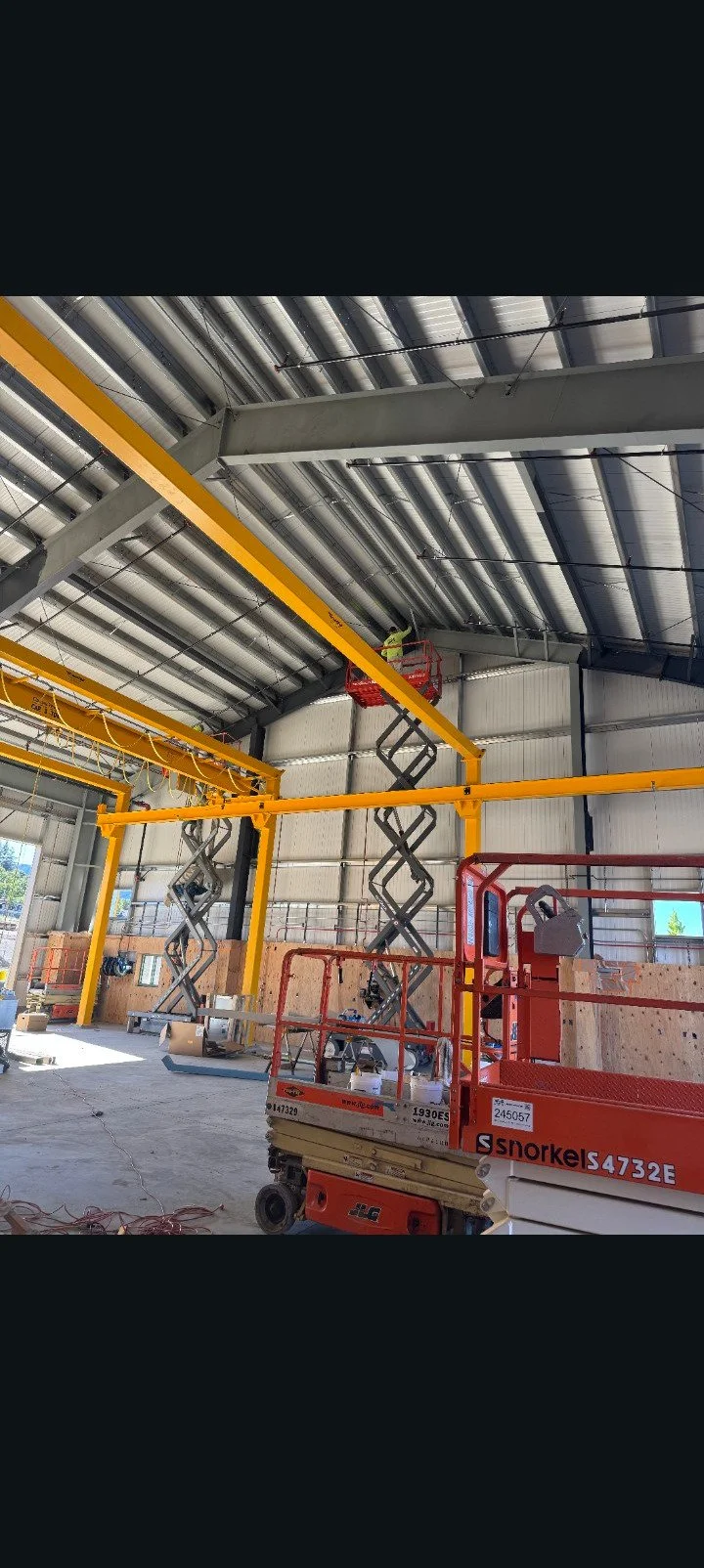 Construction workers using scissor lifts to work on ceiling supports in an industrial building under construction.