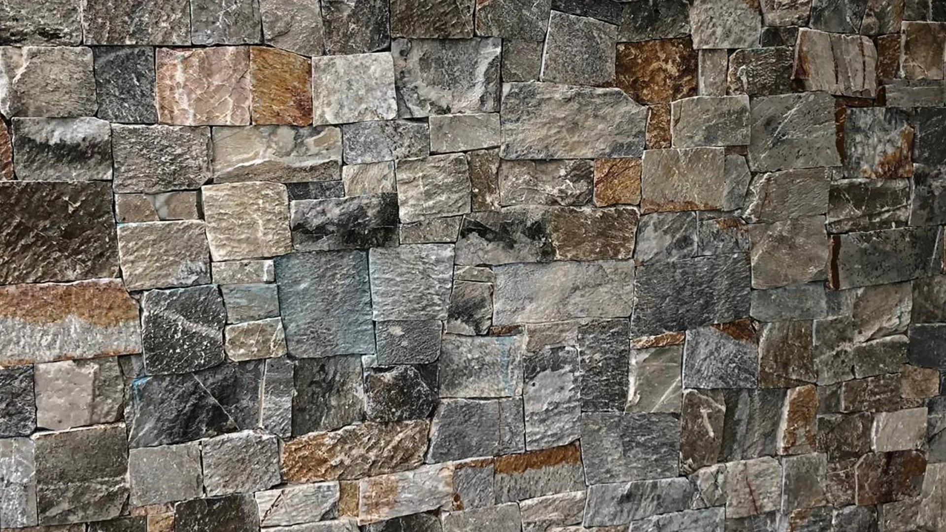 Close-up of a stone wall composed of variously sized rectangular and irregularly shaped stones in shades of gray, brown, and tan.